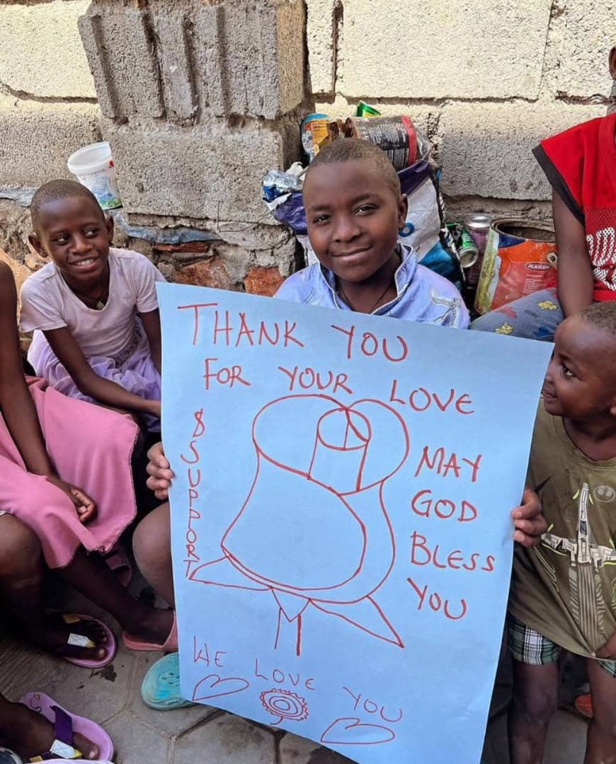 Children holding a hand-drawn sign that reads: Thank you for your love, may God bless you